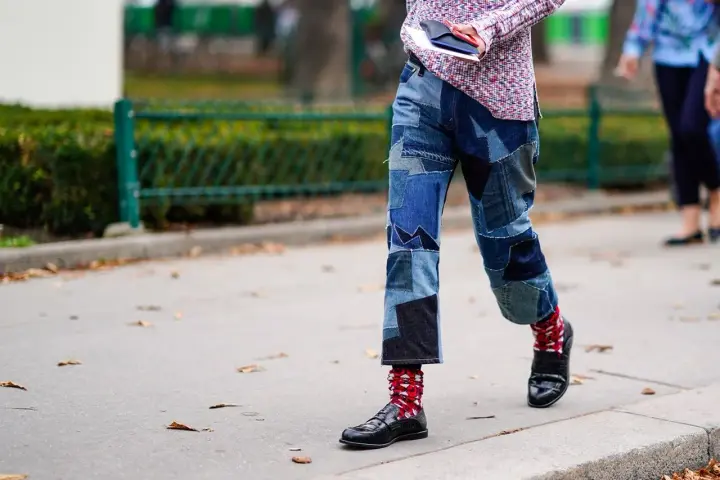 Uomo con jeans patchwork e mocassini neri, calzini rossi a fantasia.