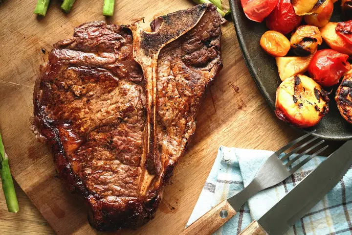 Un succulent côte de bœuf grillé, accompagné d'asperges et de tomates rôties, prêt à être dégusté.