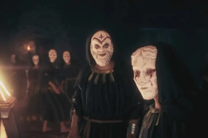 Miembros del culto de Kosmos, con túnicas oscuras y máscaras blancas, se reúnen ante un objeto piramidal brillante.