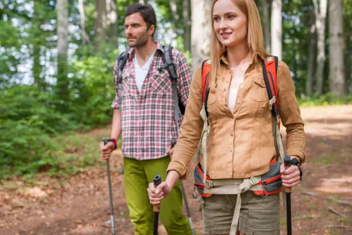 Ein Paar wandert achtsam durch einen Wald. Die Frau und der Mann nutzen Wanderstöcke, eine Anleitung für einen achtsamkeitsspaziergang.