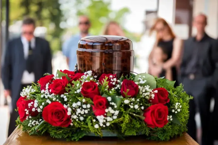 Czerwone róże i gipsówka otaczają urnę. Takie kwiaty na pogrzebie starszej osoby symbolizują miłość i pamięć.