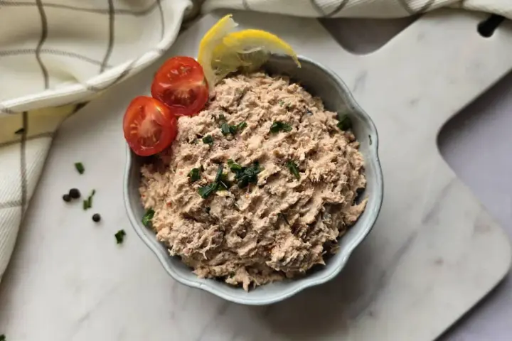 Un bol de rillettes de thon, garni de tomates cerises et de quartiers de citron, prêt à être dégusté.