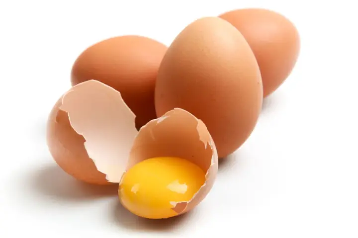 Huevos marrones, uno roto mostrando la yema brillante. ¡Un manjar que los perros pueden comer!