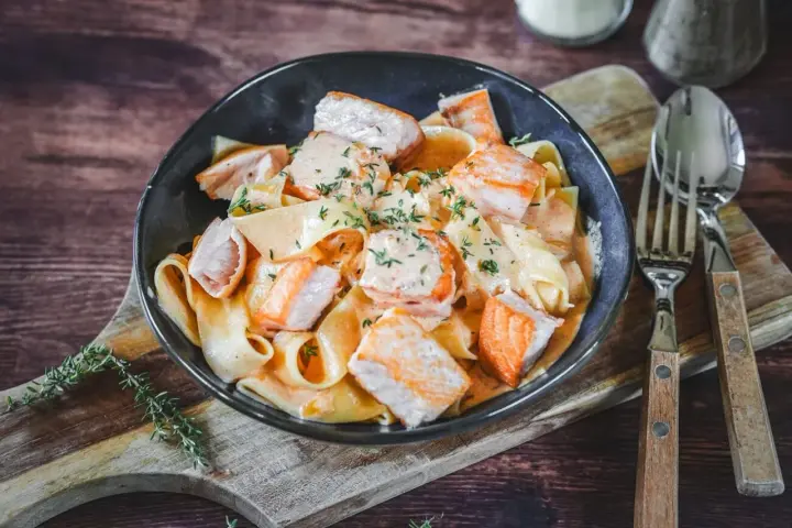 Breite Bandnudeln mit saftigen Lachs-Stücken in cremiger Lachs Sahne Sauce, garniert mit frischen Kräutern. Ein Genuss!