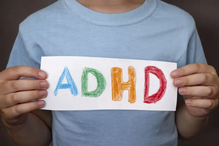 Mani di bambino tengono un foglio con la scritta "ADHD" colorata. Riconoscere i sintomi dell'ADHD è il primo passo.