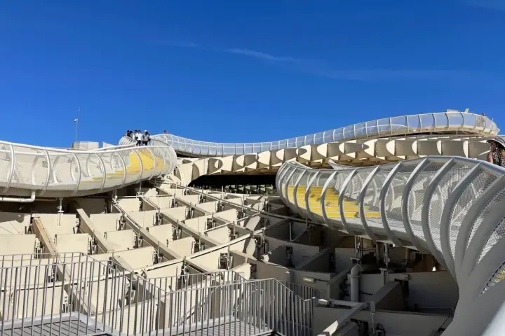The Metropol Parasol, known as Las Setas de Sevilla, features a modern wooden structure with winding walkways and yellow steps under a clear blue sky.