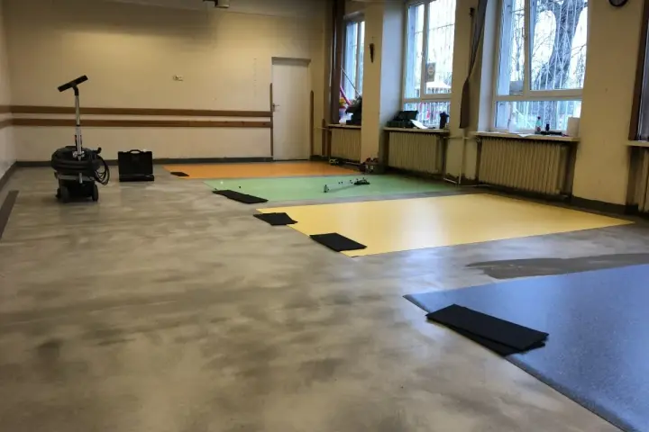 Przygotowanie podłogi pod wykładzinę PCV: odkurzacz przemysłowy i kolorowe maty czekają na ułożenie.