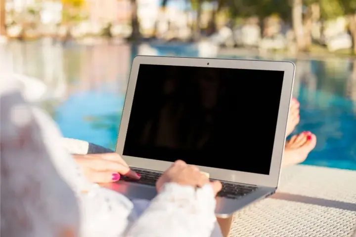 Donna lavora al laptop vicino alla piscina, godendosi l'internet temporaneo per la seconda casa.