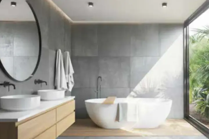 Salle de bain moderne avec baignoire îlot, double vasque et grande fenêtre donnant sur la végétation. L'étanchéité entre bac à douche et mur est assurée par des joints discrets.
