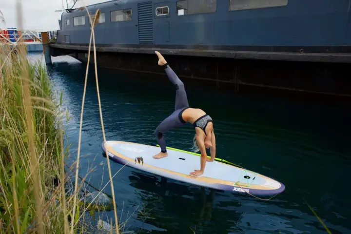 Frau macht Yoga-Brücke auf SUP-Board. Stand up paddle gesund und fördert Balance.