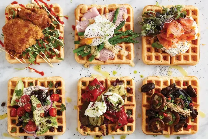 Sex olika protein våfflor: friterad kyckling, pocherat ägg med sparris, rökt lax, avokado och bönor, grillade grönsaker, och svamp.