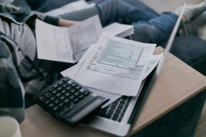 Osoba przegląda dokumenty podatkowe, kalkulator i laptop. Zastanawia się, do kiedy obowiązuje tarcza na prąd.