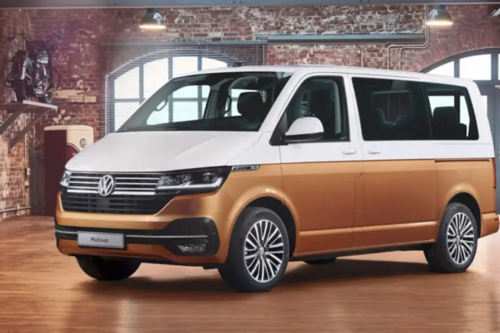 Biało-złoty bus osobowy Volkswagen Multivan w garażu z ceglaną ścianą.