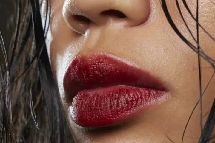 Labbra sensuali con rossetto ciliegia, un colore audace che esalta la bellezza naturale. Capelli bagnati e pelle luminosa completano il look.