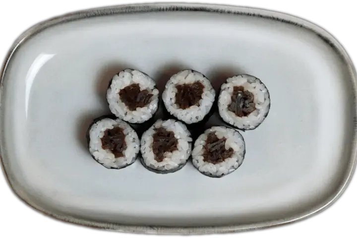 Sześć kawałków sushi z ryżem i ciemnym nadzieniem na szarej tacy.
