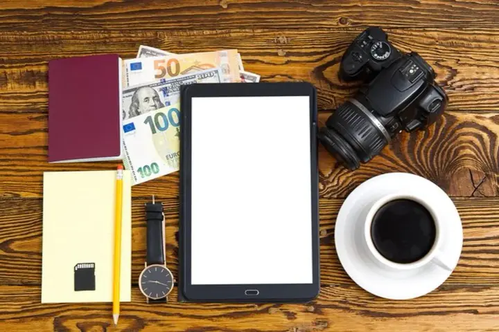 Planujesz podróż? Zastanawiasz się, ile kosztuje zdjęcie do dowodu u fotografa? Na zdjęciu paszport, pieniądze, aparat i tablet.
