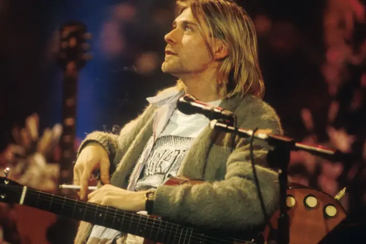 Kurt Cobain z papierosem w dłoni, grający na gitarze. Jego muzyka to część 100 najlepszych piosenek wszechczasów.