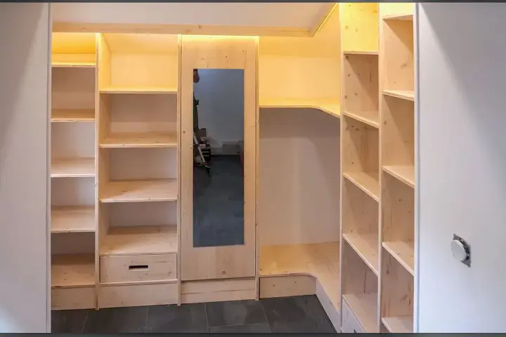 Construction d'une armoire sur mesure avec des portes coulissantes et des étagères en bois clair. Un miroir est intégré.