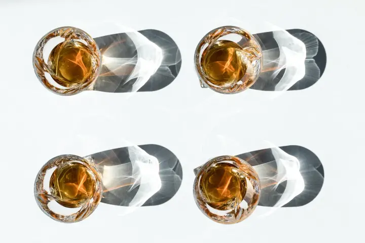 Vier Gläser mit bernsteinfarbenem Whisky werfen dramatische Schatten. Ein visueller Vergleich, der den Unterschied Scotch und Bourbon verdeutlicht.