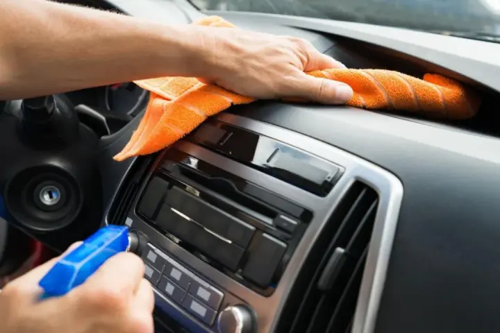 En hand sprayar och torkar av bilens instrumentbräda med en orange trasa. Det ser ut som en magisk rengöring för att få bilen skinande ren.