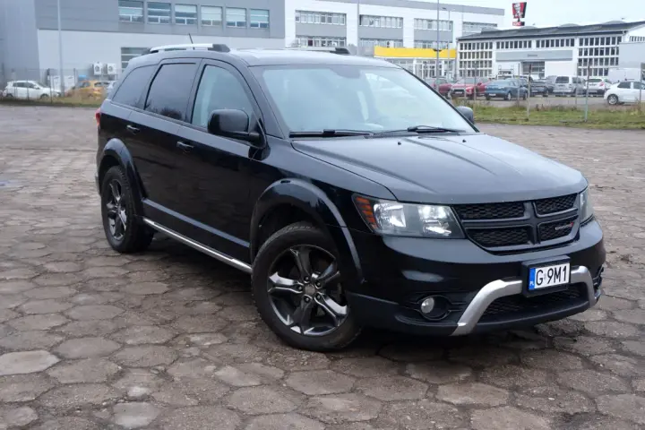 Czarny Dodge Journey 3.6 zaparkowany na placu z kostki brukowej. W tle budynki i inne samochody.