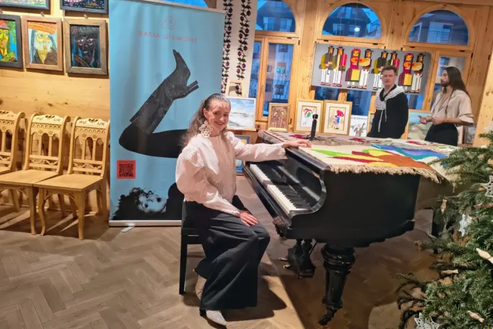 Młoda artystka przy pianinie, gotowa do wykonania piosenki "zimna woda". W tle baner z jej imieniem i nazwiskiem.