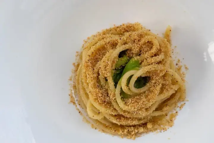 Spaghetti conditi con aglio, olio e peperoncino, cosparsi di pangrattato croccante e qualche foglia verde.