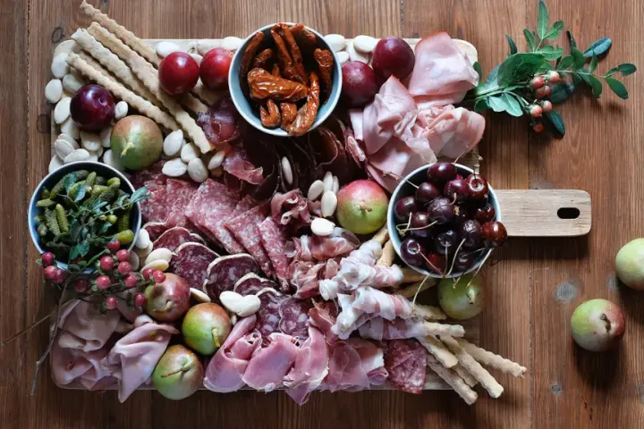 Un invitante tagliere fai da te con salumi, formaggi, frutta, sottaceti e grissini, pronto per essere gustato.