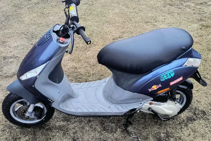 Niebieski skuter z naklejkami Red Bull i Motul na tle trawy.
