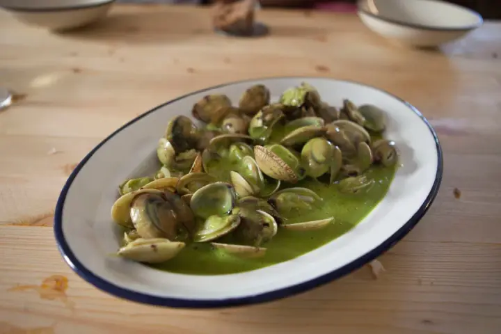 Almejas en salsa verde, un plato delicioso y fresco, servido en una cazuela sobre una mesa de madera.