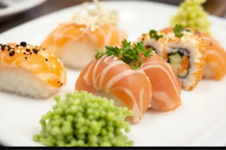 Talerz z różnorodnym nigiri sushi z łososiem, posypane sezamem i ozdobione natką pietruszki. Obok porcja zielonego wasabi.