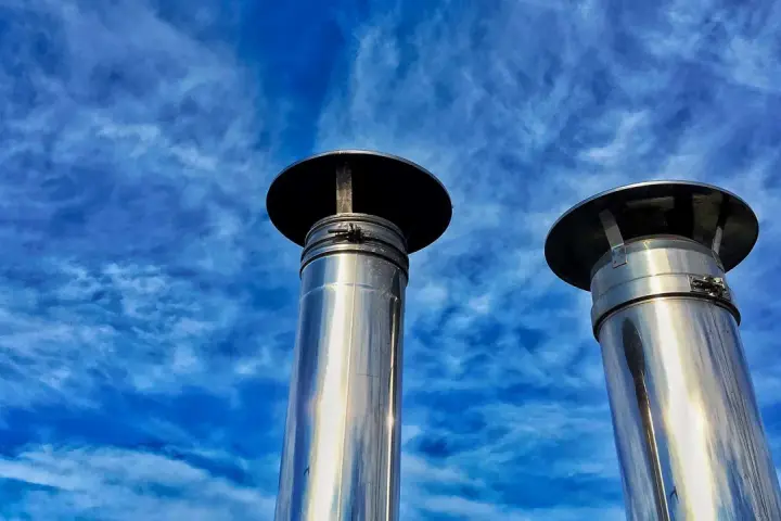 Due camini in acciaio inox, modello uni 7129 scarico a parete, brillano sotto un cielo blu con nuvole sottili.