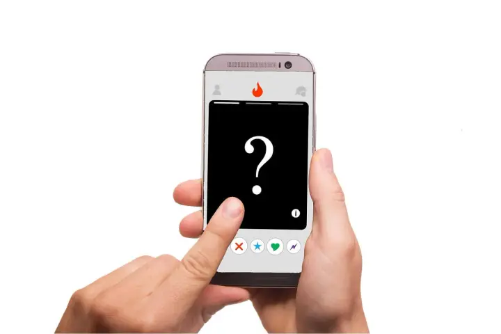 Dłoń trzyma smartfon z aplikacją randkową. Na ekranie widnieje znak zapytania i ikony: X, gwiazdka, serce, błyskawica. To **Tinder oznaczenia** – decyzja należy do Ciebie!
