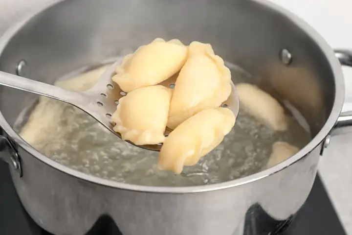 Pierogi gotujące się w garnku, wyjmowane łyżką cedzakową.