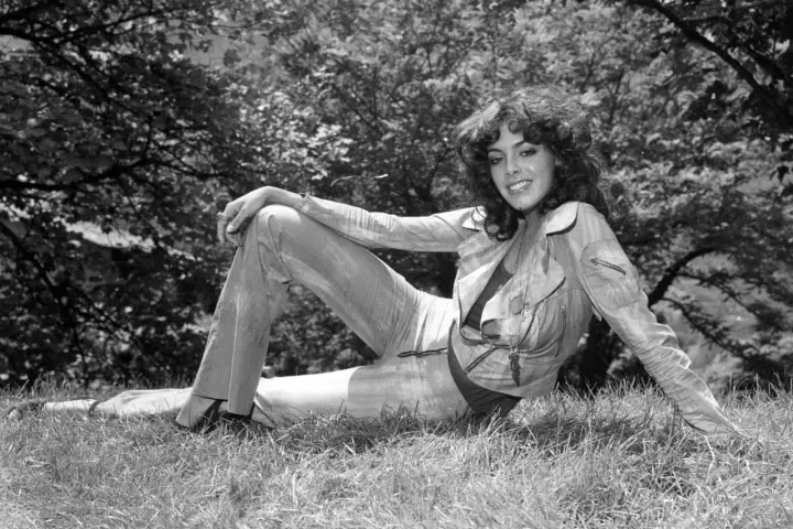 Nadia Cassini, con il suo fisico prorompente, posa su un prato, sfoggiando un completo giacca e pantaloni.