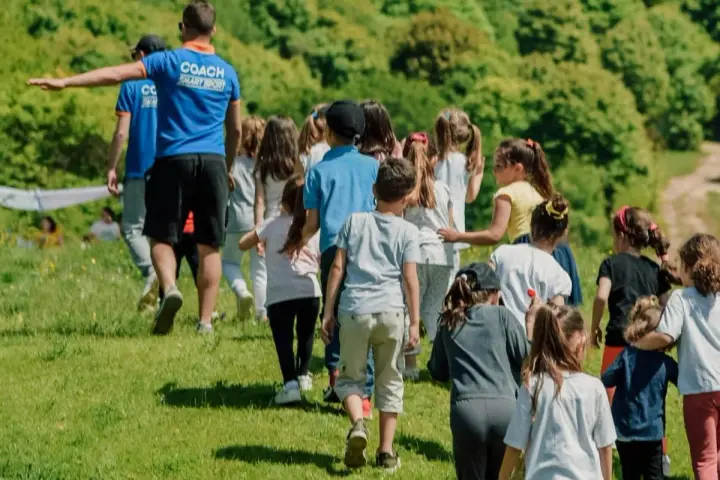 Un groupe d'enfants suit un coach sur une colline verdoyante. Ces actions pour financer un voyage scolaire sont pleines d'énergie et de joie.