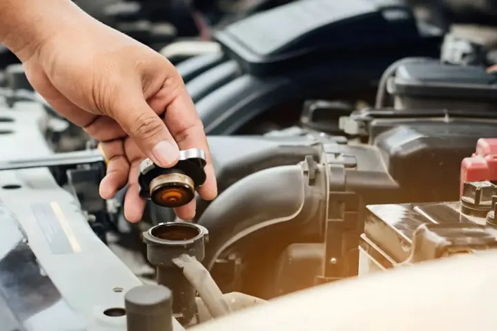 Hand removing radiator cap. This image might be relevant when researching radiator hose replacement cost.