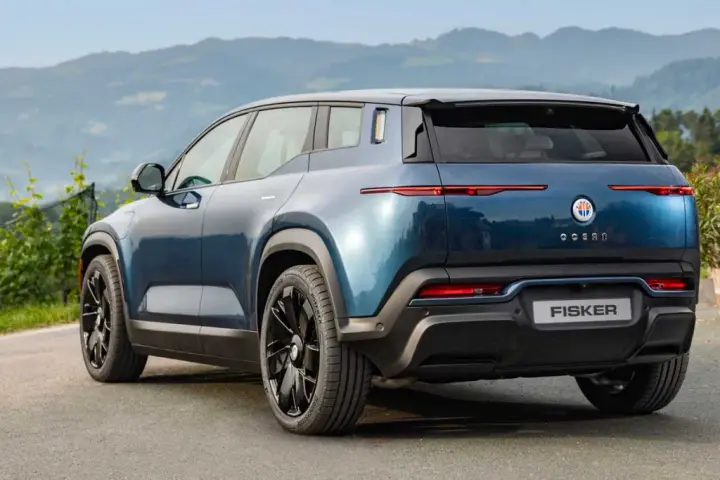 Tylna część niebieskiego elektrycznego SUV-a Fisker Ocean na tle gór i zieleni.