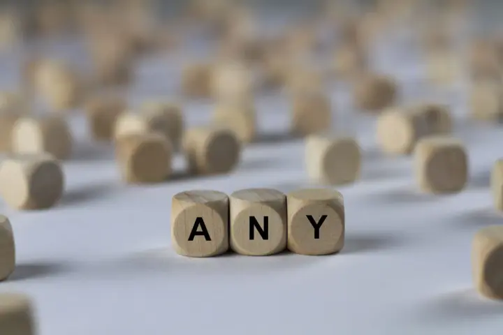 Holzwürfel mit den Buchstaben A, N, Y bilden das Wort "ANY". Sie liegen auf einem hellen Untergrund, umgeben von vielen weiteren unscharfen Würfeln.