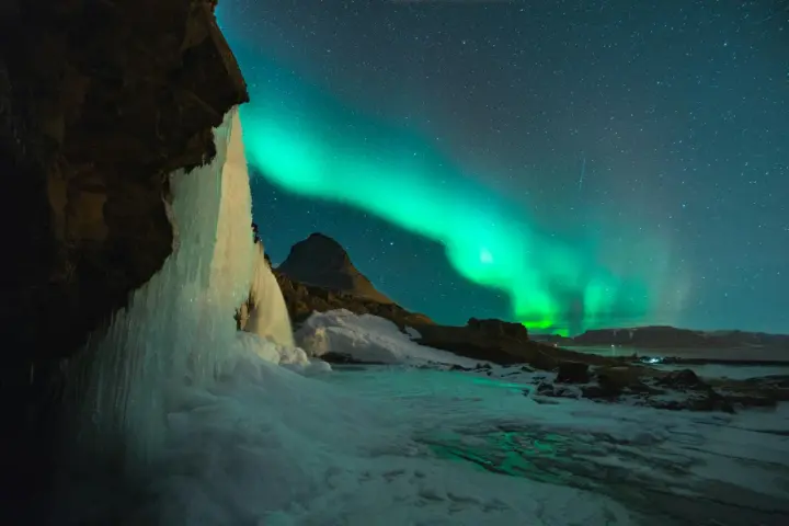 Lodowy wodospad i zorza polarna na nocnym niebie. Islandia w styczniu, magiczny widok.