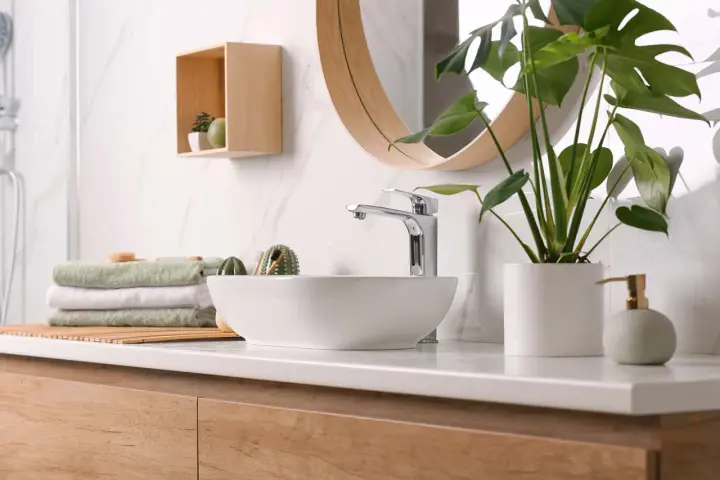 Plan de travail de salle de bain moderne avec vasque, robinetterie chromée, serviettes pliées et plante verte. La hauteur du plan de travail est idéale.