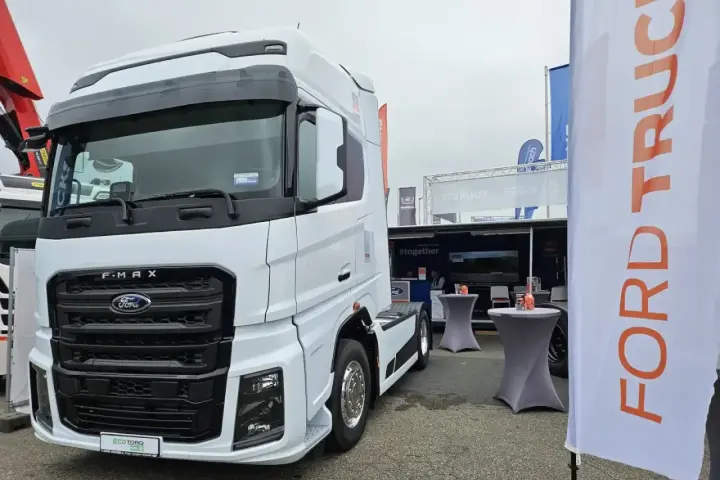 Biały Ford F-MAX prezentuje się na wystawie, obok banerów z logo Ford Trucks.