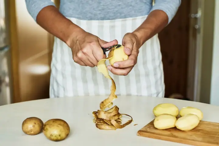 Mani che sbucciano patate per la cottura. Il tempo di cottura patate lesse senza buccia è breve.