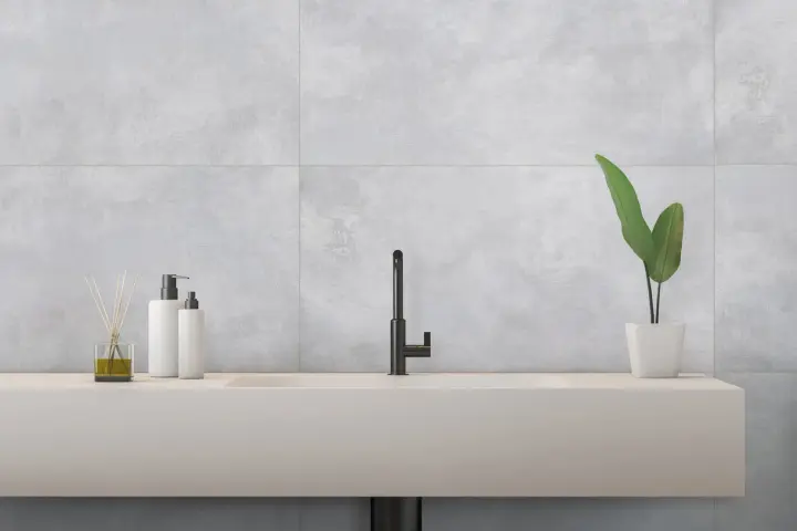 Évier moderne avec robinetterie noire, flacons de savon et plante verte, sur un mur en carrelage rectifié gris.
