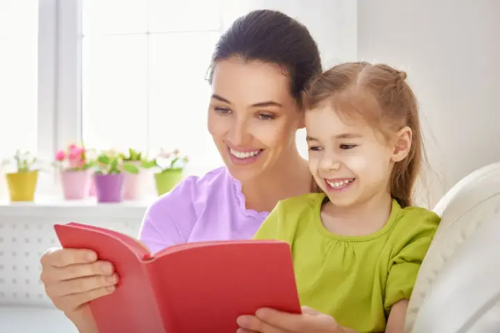 Uśmiechnięta mama czyta bajkę córce. To wspaniała opieka na dziecko 2 dni w tygodniu, pełna radości i wspólnych chwil.