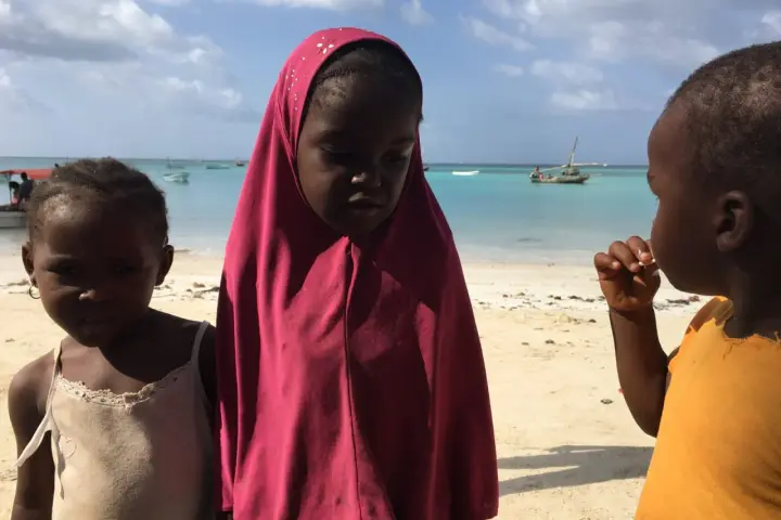 Dzieci na plaży, w tle turkusowe morze i łodzie. To obrazek z życia na Zanzibarze.