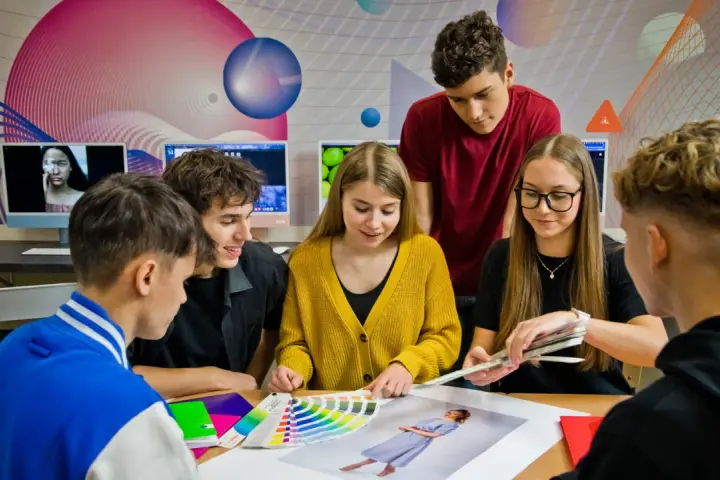 Grupa młodych ludzi dyskutuje nad próbkami kolorów i zdjęciami przy biurku.