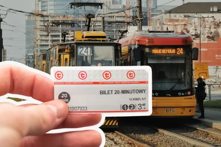 Warszawski bilet 20 minutowy w dłoni, na tle tramwajów i miejskiej zabudowy.