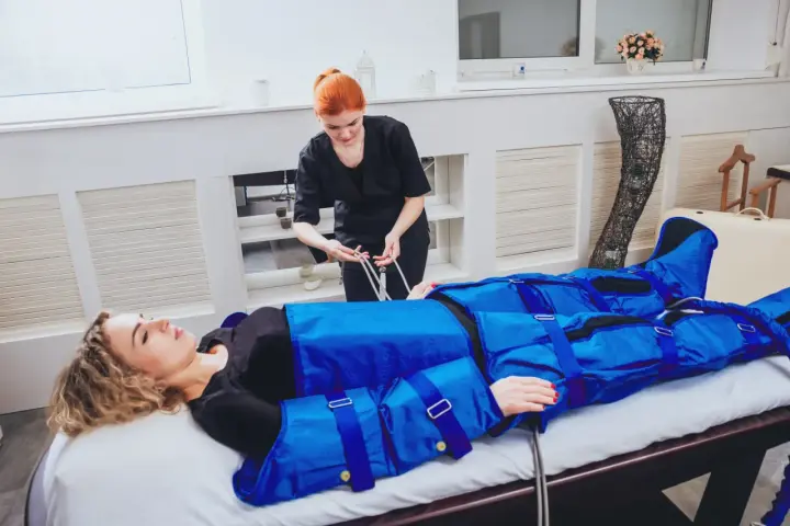 Kobieta w salonie piękności przechodzi zabieg drenażu limfatycznego. Terapeuta przygotowuje urządzenie do masażu uciskowego.