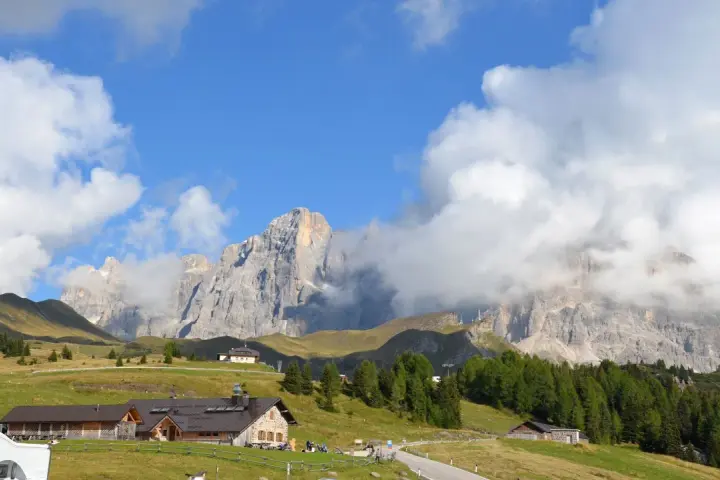Panorami mozzafiato per escursioni a Passo Rolle. Rifugi alpini e vette imponenti sotto un cielo azzurro con nuvole bianche.